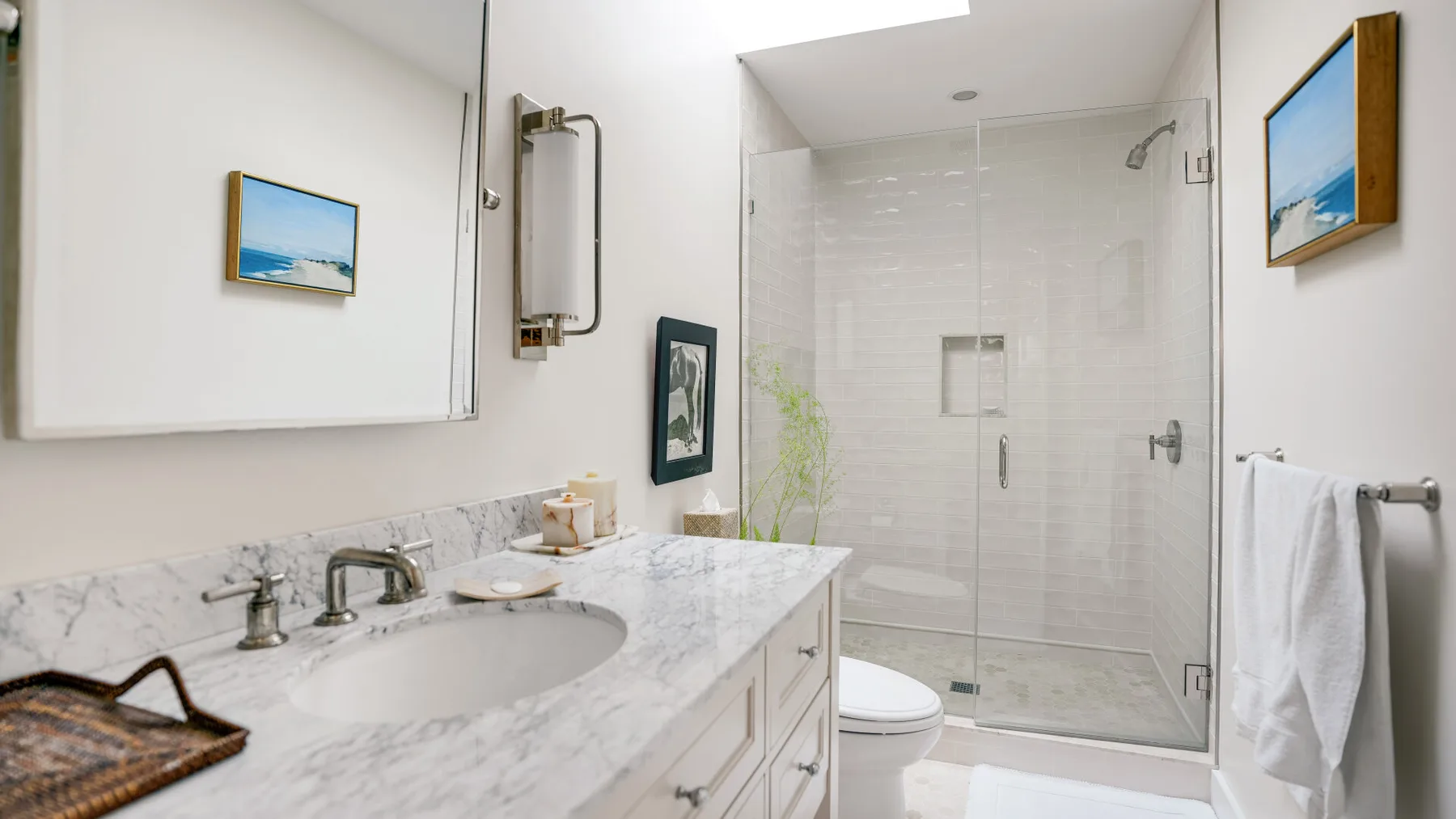 A bright bathroom with a marble vanity and glass shower.