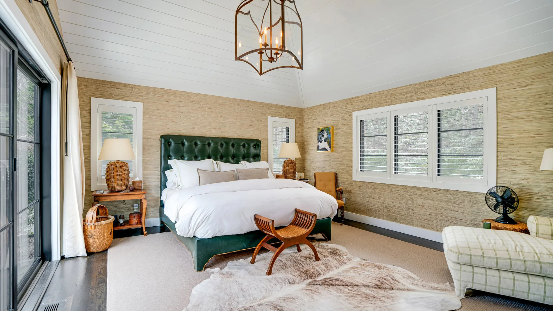 A bedroom with a green upholstered bed, a large window, and an armchair.
