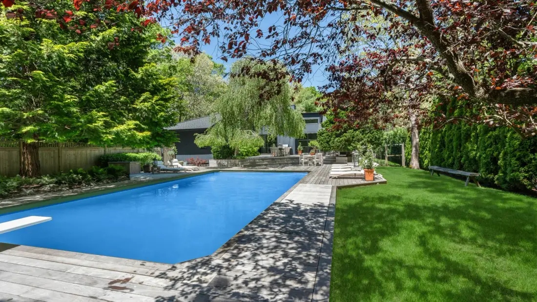An outdoor swimming pool beside a green lawn and leafy trees.