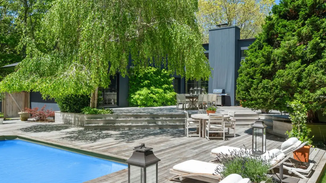 Un patio ajardinado con terraza de madera, asientos y piscina.