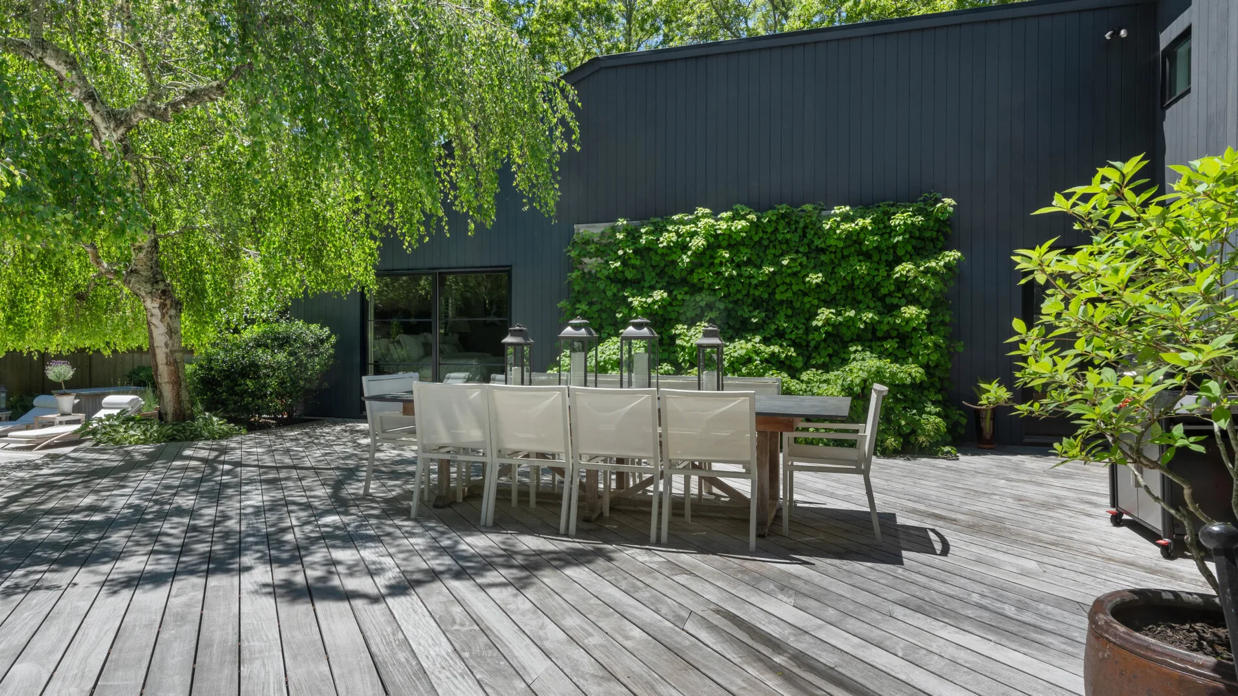 An outdoor dining area with a long table and seating beside a leafy garden.
