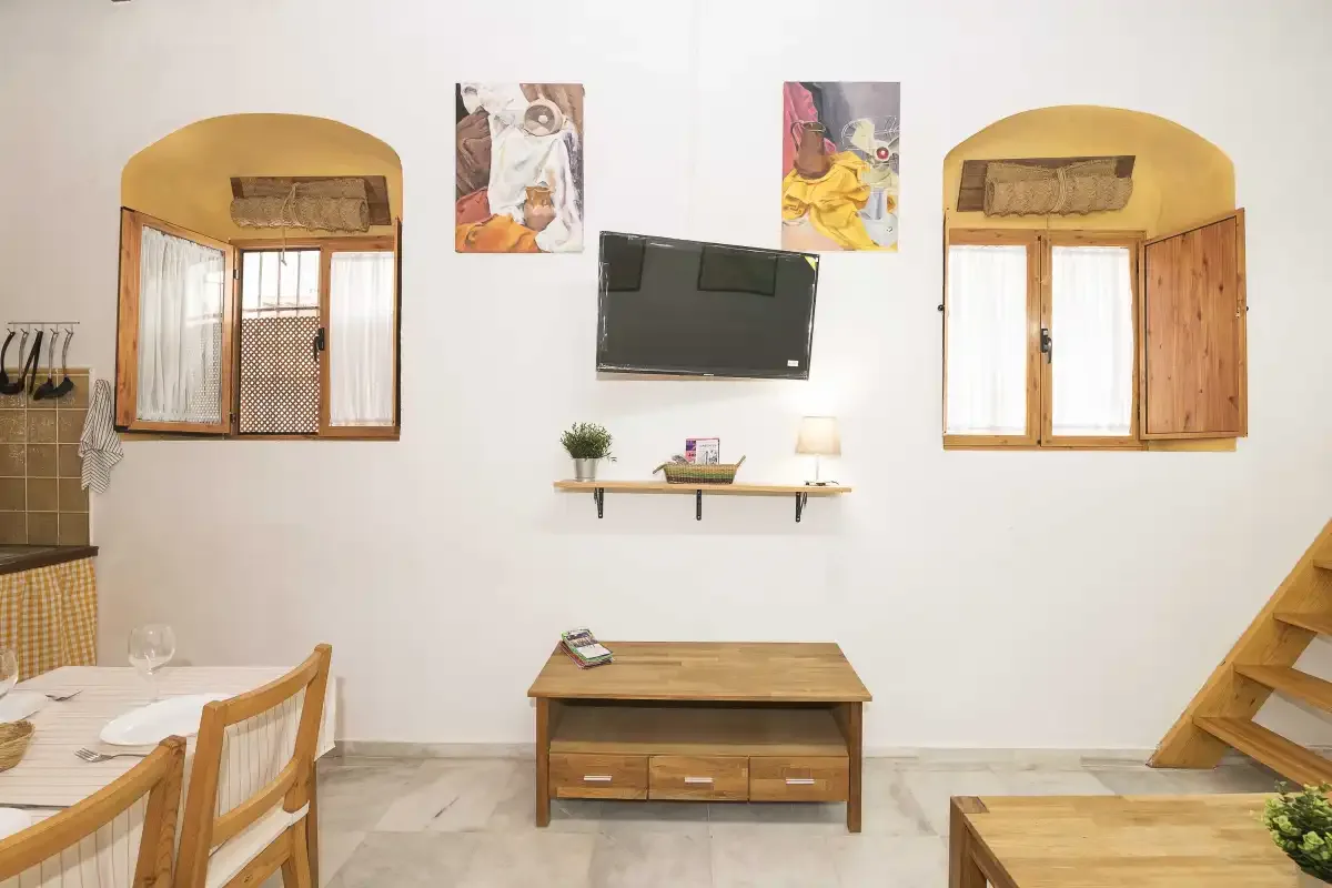 A bright living and dining area with a wall-mounted television and wooden furnishings.