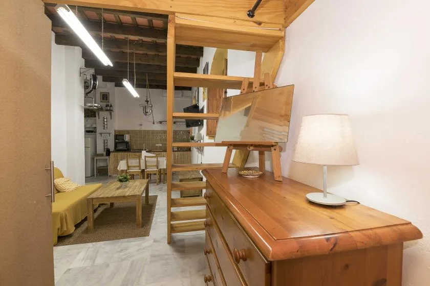 Una sala amueblada con una escalera de madera y un escritorio con una lámpara.