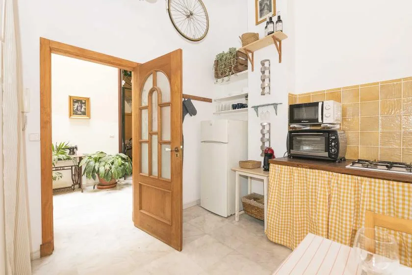 A bright kitchen with a refrigerator, countertop appliances, and an open wooden door.