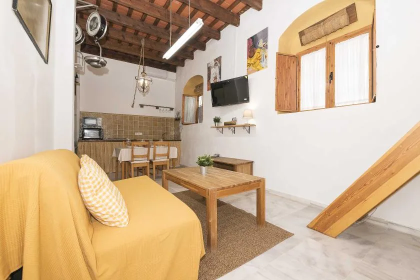 A living area with yellow seating, a wooden coffee table, and a compact kitchen.