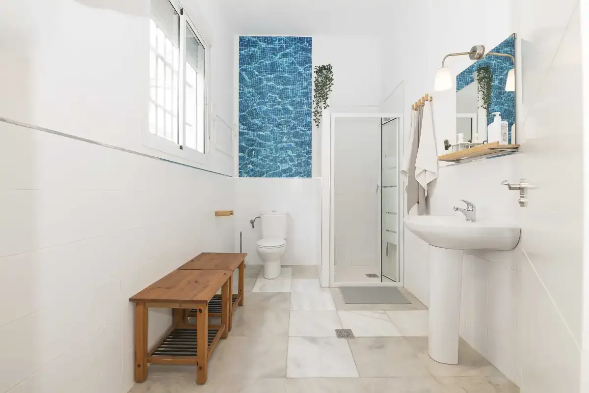 A bright bathroom with a shower, sink, and wooden bench.