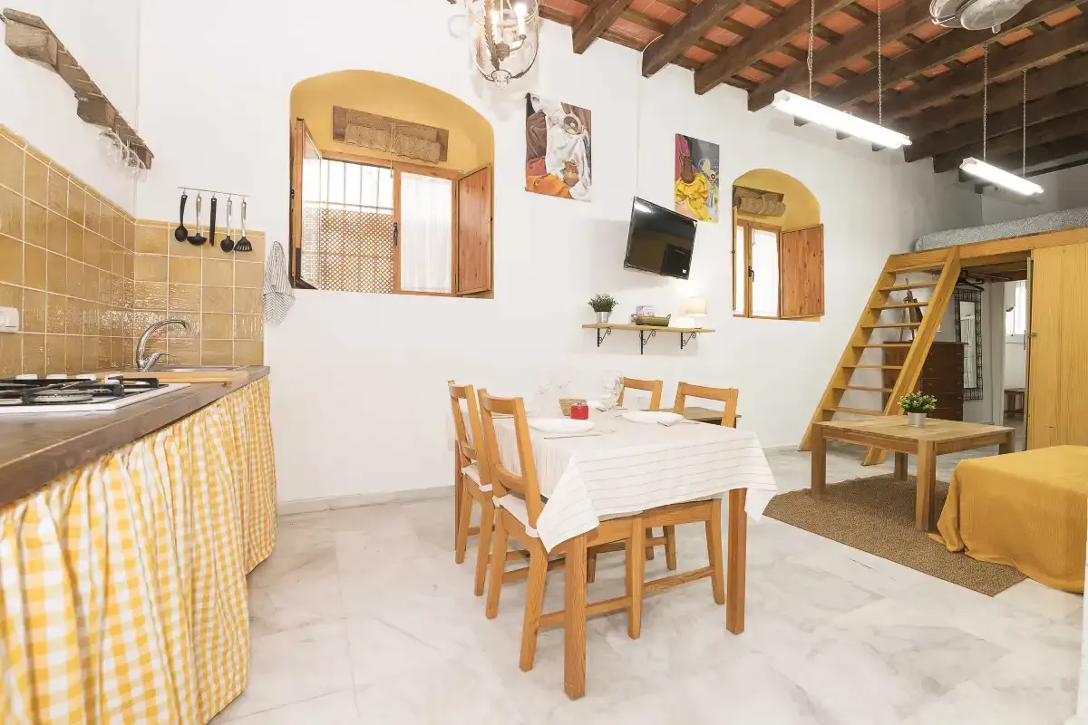 A combined kitchen and dining area has a wooden table beneath exposed ceiling beams.