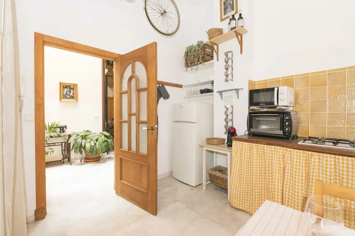 A small kitchen with a refrigerator, microwave, and checkered counter curtain.