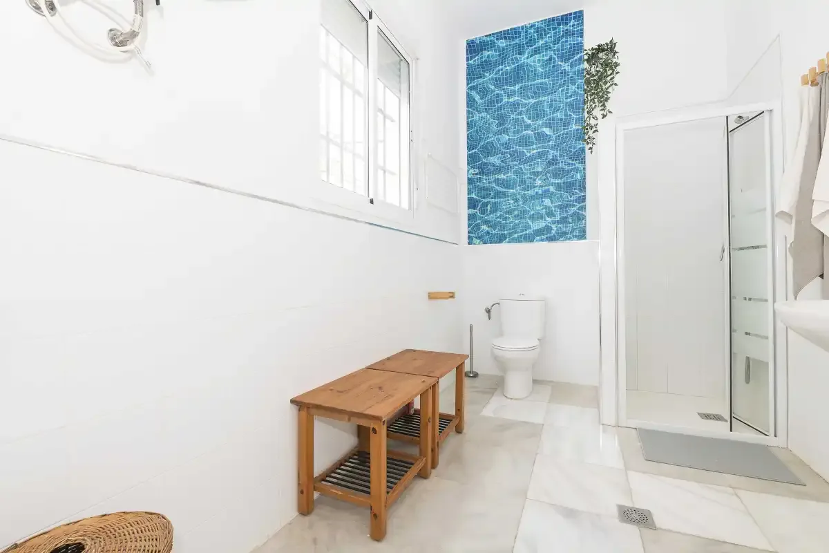 A bright bathroom with a toilet, wooden bench, and shower.