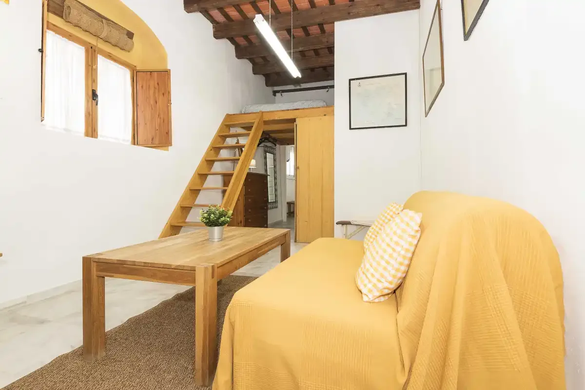 A bright loft living area with yellow seating, a wooden table, and stairs.