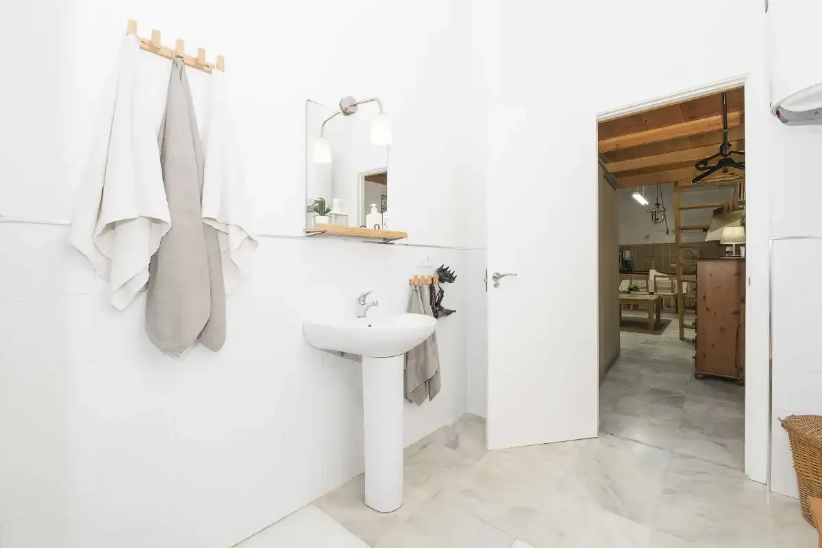 A bright bathroom with a wall-mounted sink and towels beside an open doorway.