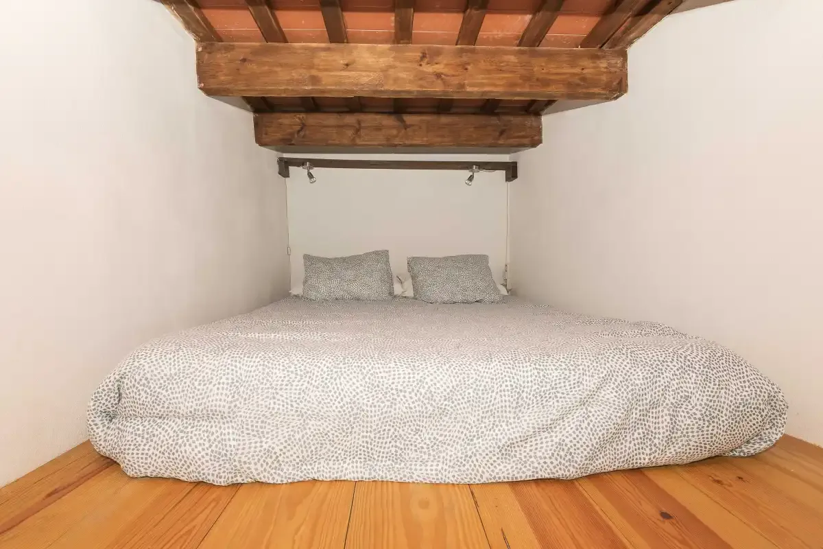 A low bedroom with a large bed beneath exposed wooden ceiling beams.