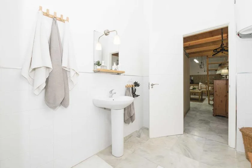 A bright bathroom with a pedestal sink and an open doorway.
