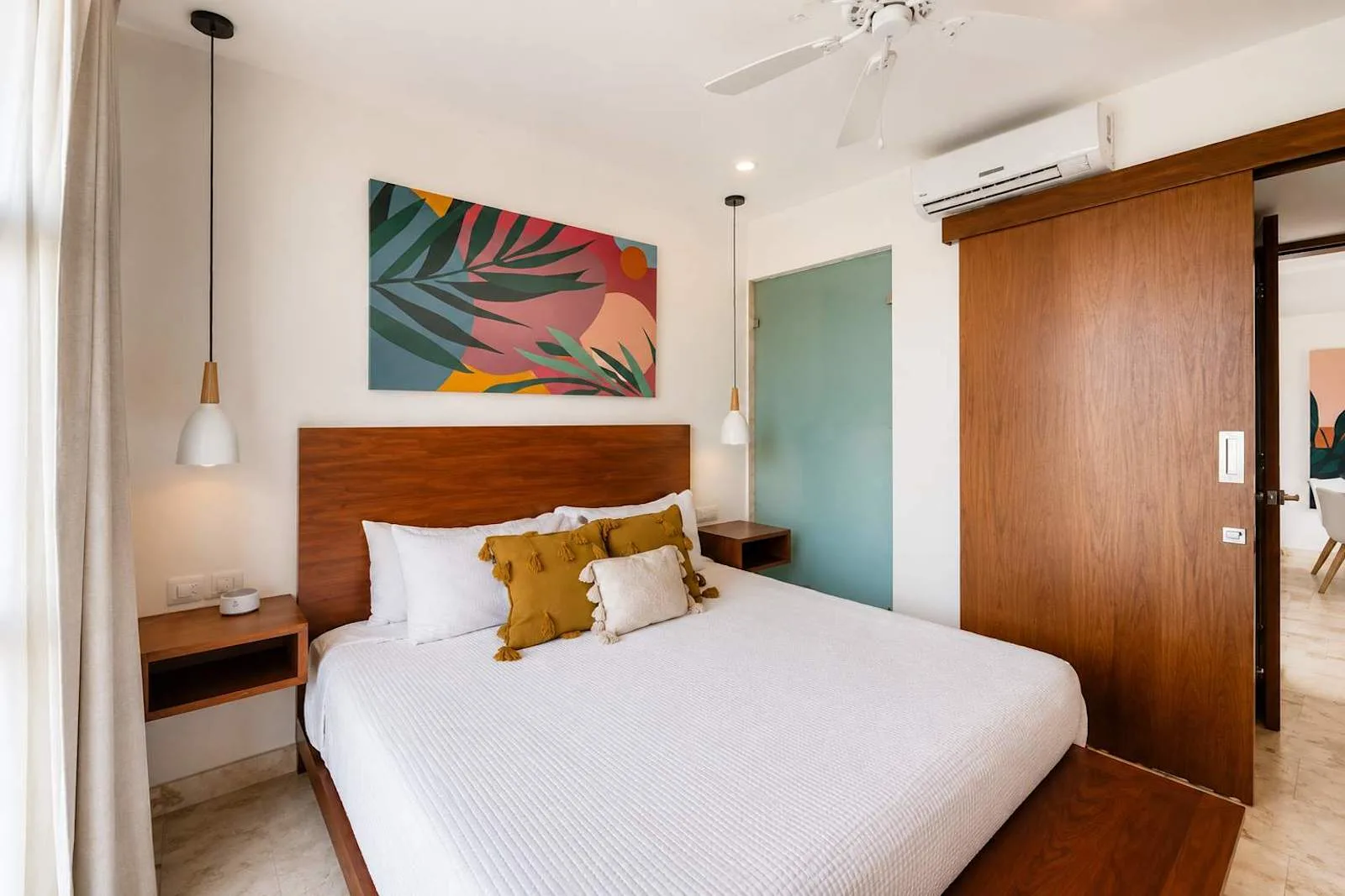 Dormitorio con una cama bien arreglada y una colorida obra de arte sobre el cabecero.