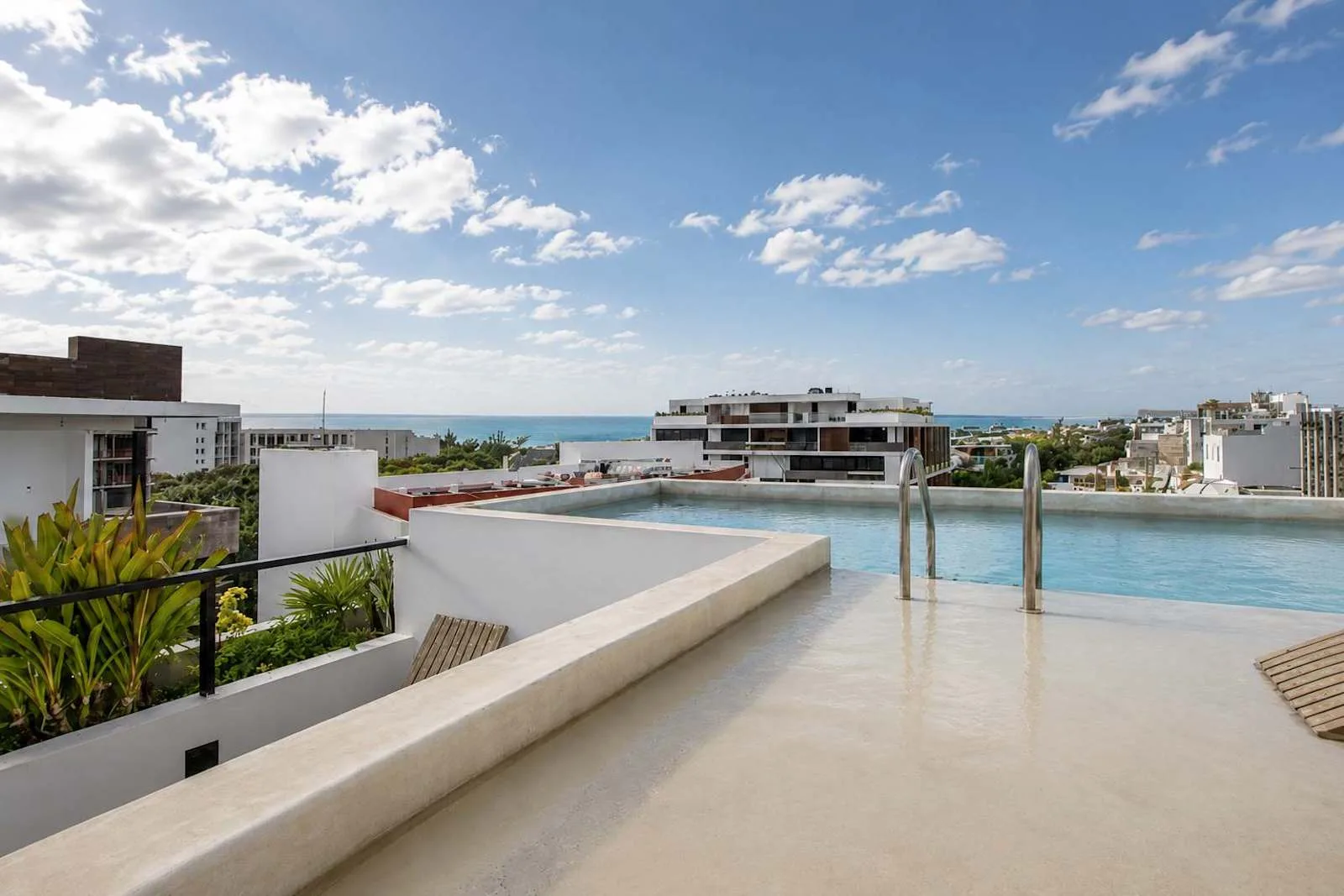 Una piscina en la azotea domina edificios cercanos y el mar bajo un cielo parcialmente nublado.