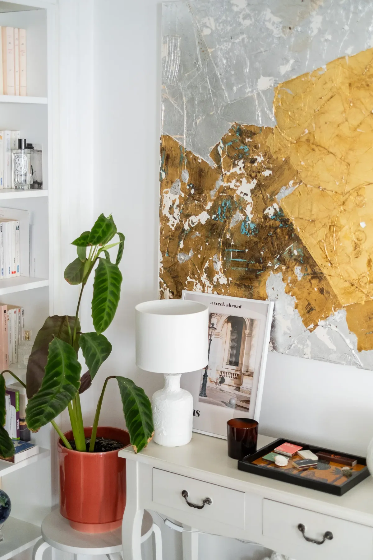 Un rincón interior luminoso muestra una consola blanca, una planta frondosa y arte abstracto.