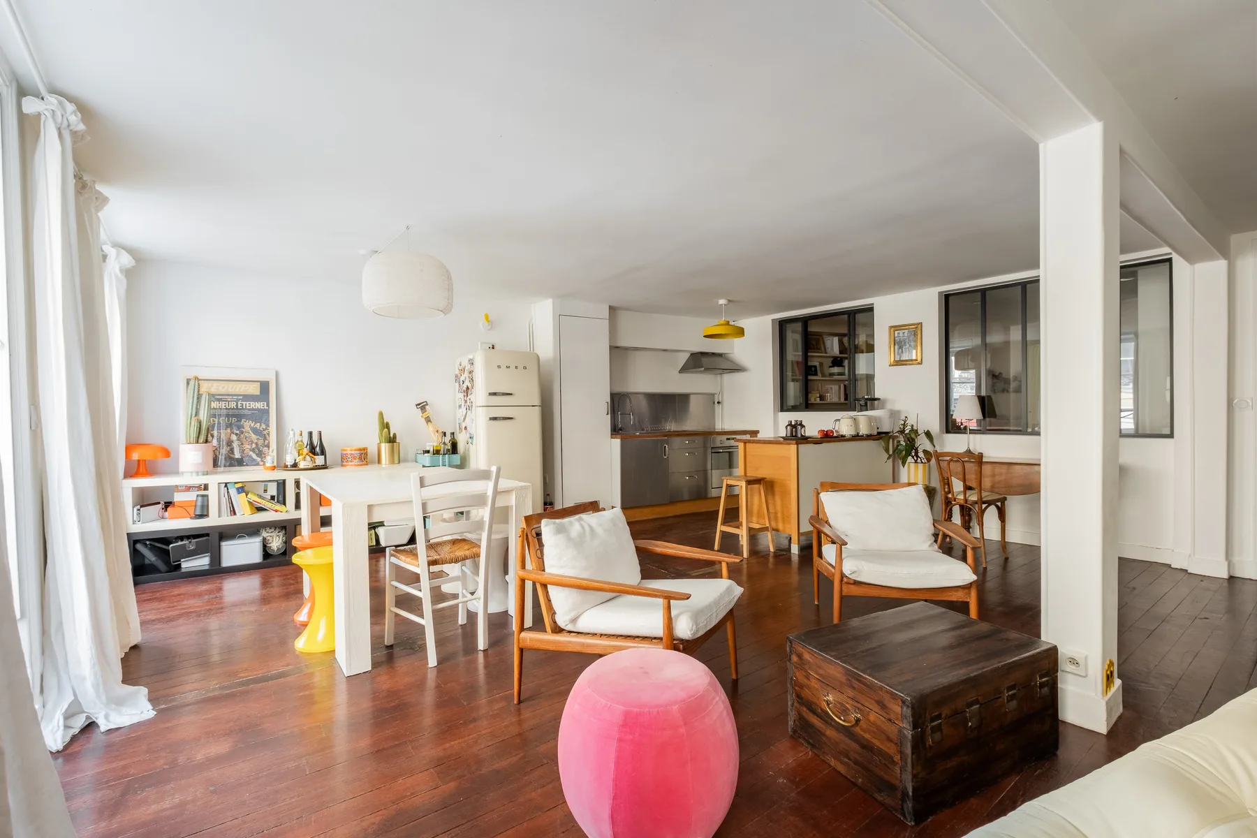 Una luminosa sala de estar y comedor de planta abierta tiene suelo de madera y una cocina al fondo.