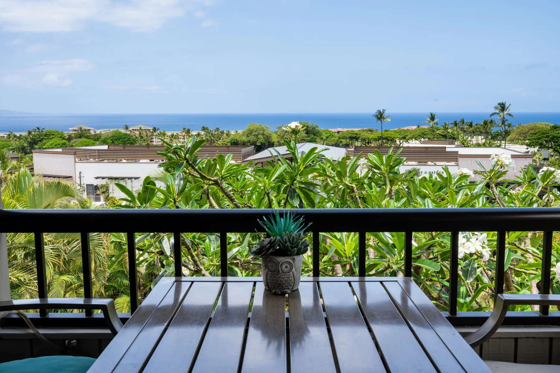 A balcony dining area overlooks tropical greenery and the ocean.