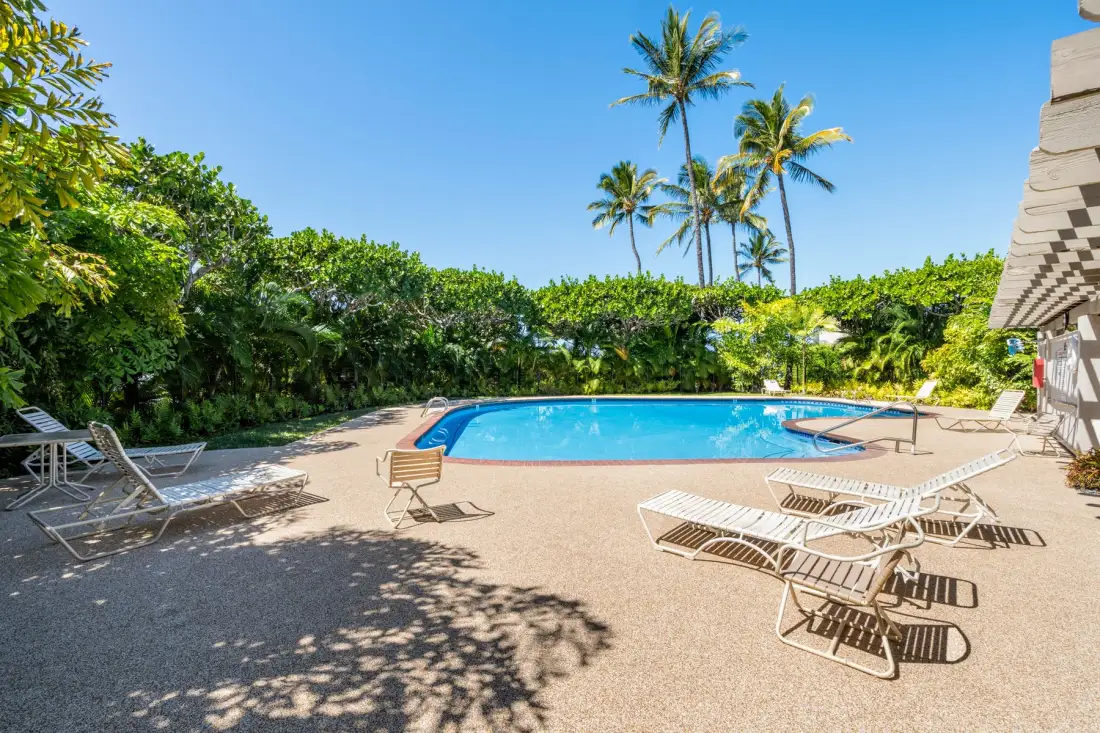 An outdoor swimming pool is surrounded by lounge chairs and tropical greenery.
