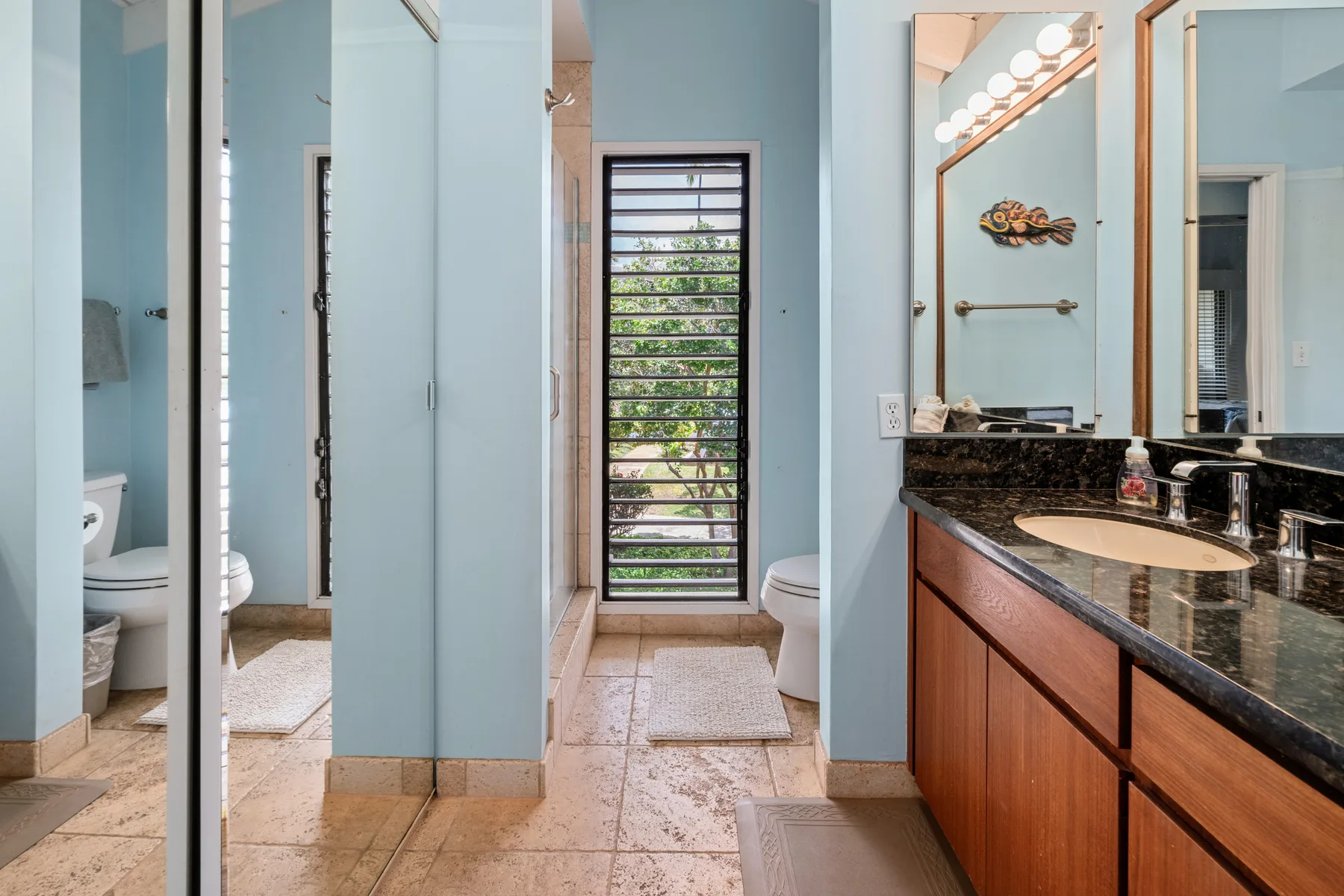 A bathroom with a long vanity, mirrors, and a narrow window.