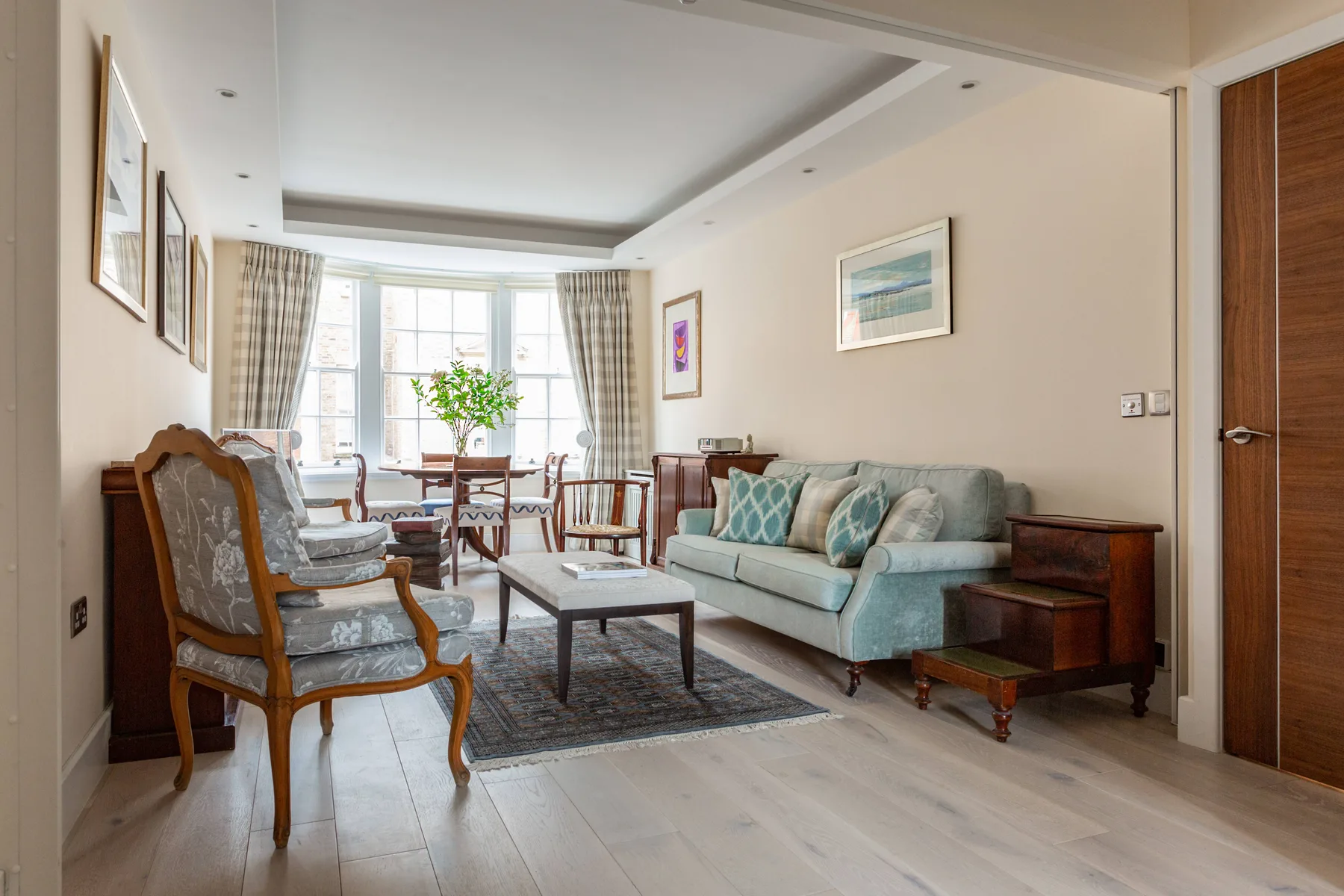 A bright living room with seating around a coffee table and a dining area by the windows.