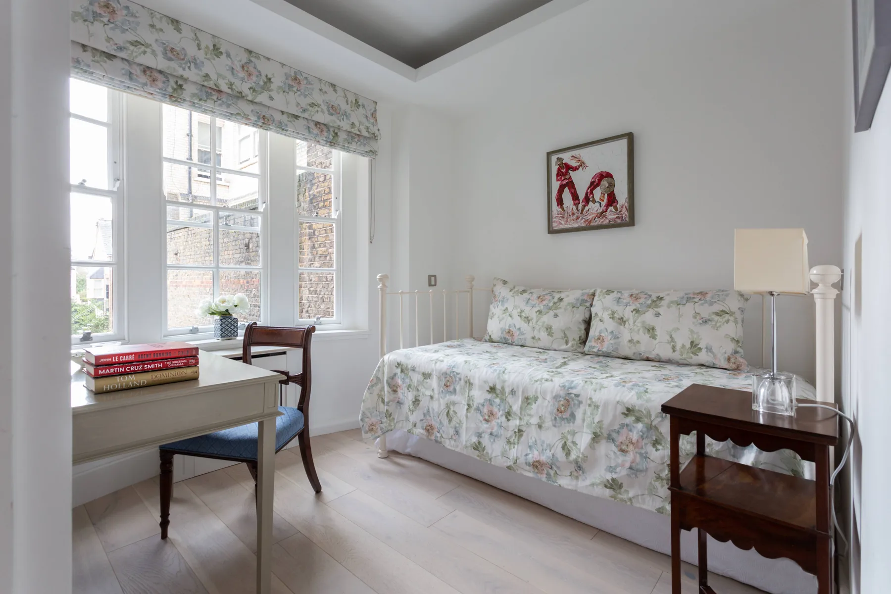 A bright bedroom with floral bedding, a desk, and a large window.