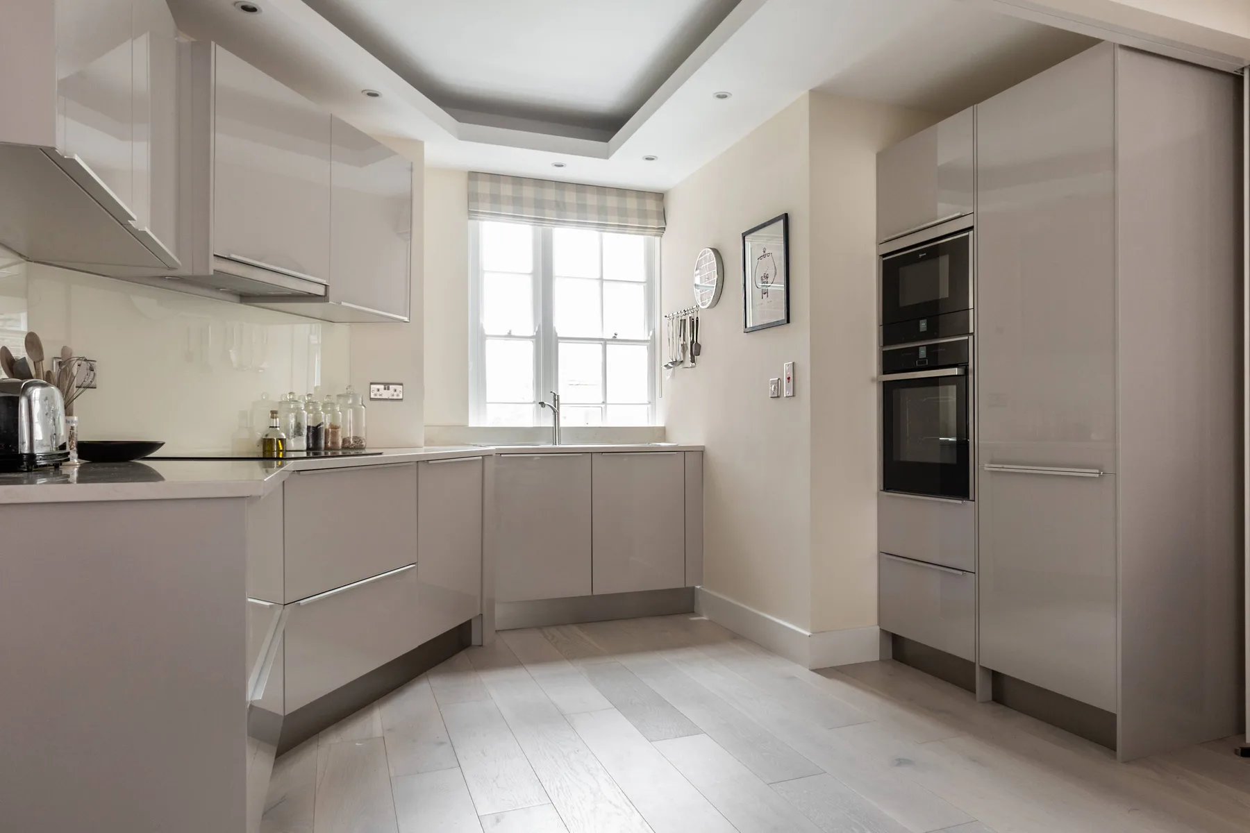 A modern kitchen with pale cabinets, a central window, and built-in appliances.