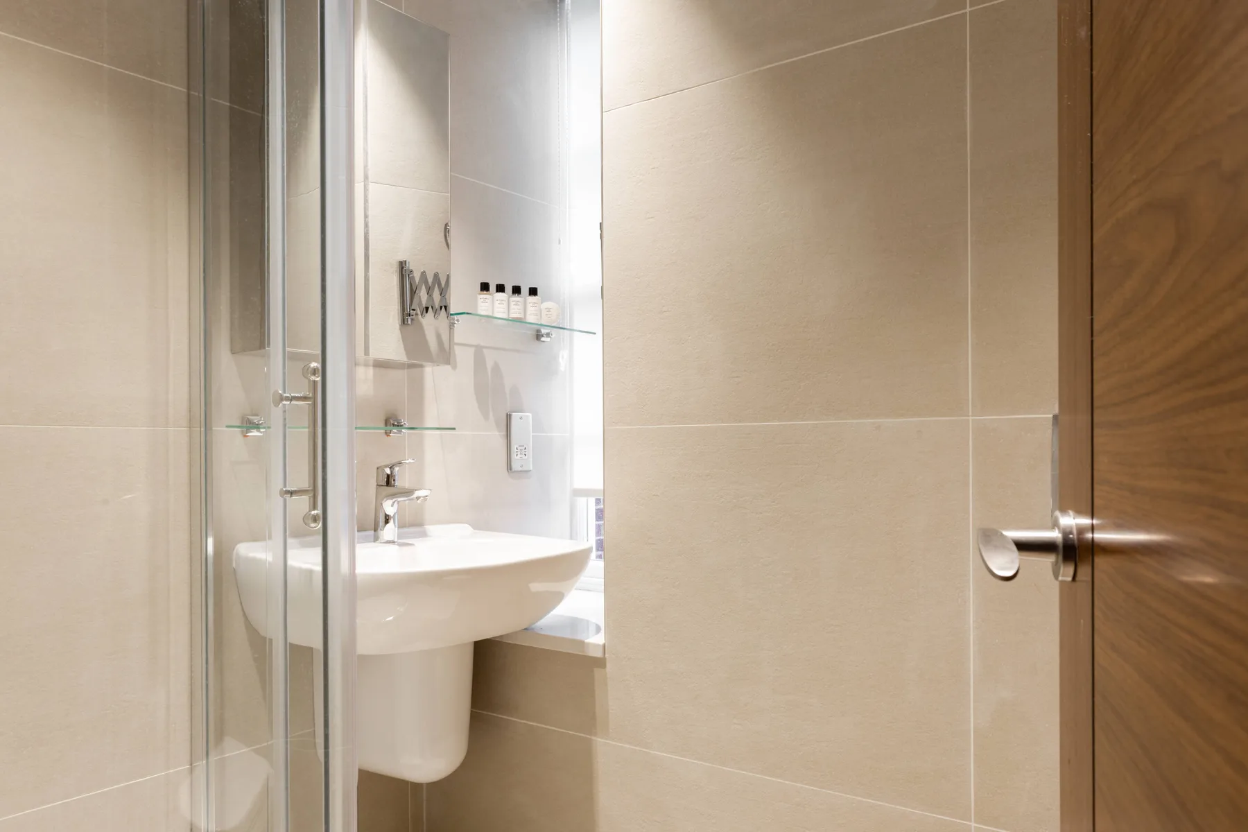 A tiled bathroom with a white sink, glass shower, and wooden door.