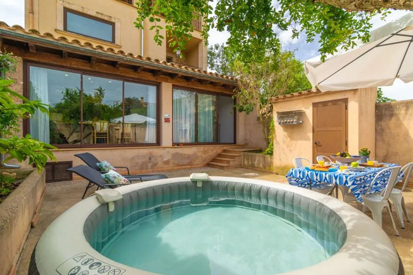 A patio with a round hot tub, outdoor seating, and a table beneath a large umbrella.