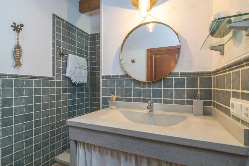 A tiled bathroom vanity with a wide sink and round wall mirror.