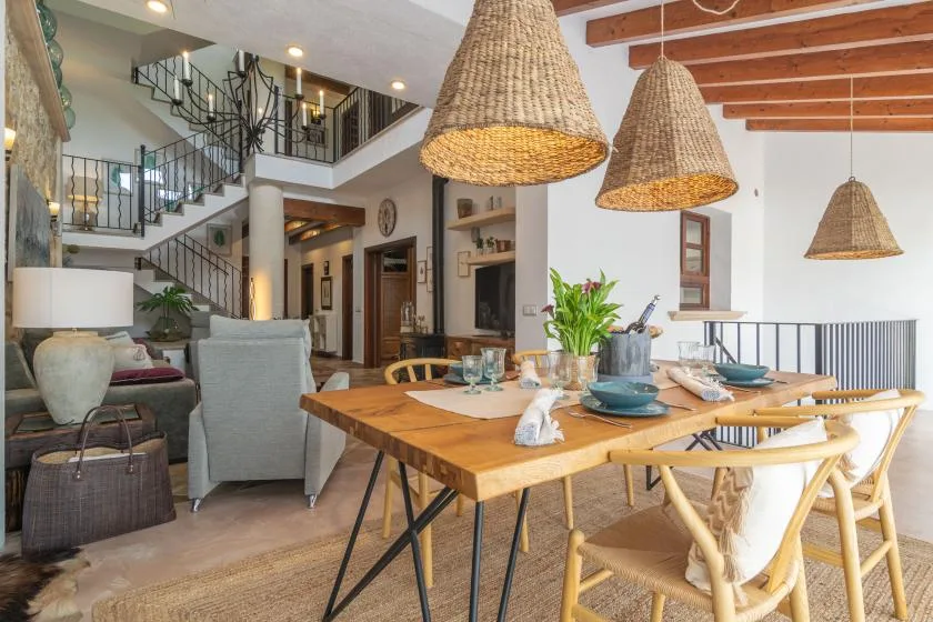 A bright dining and living area features a wooden table beneath woven pendant lights.