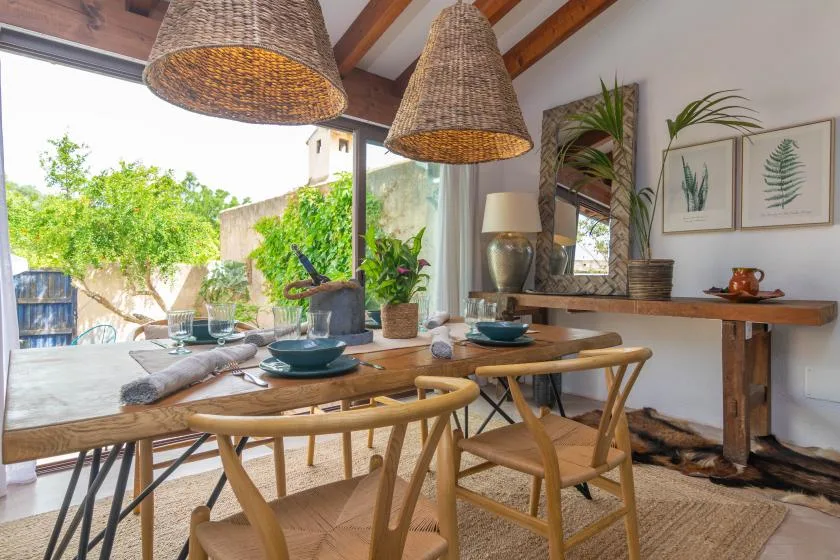 A dining area with a wooden table set beside large windows overlooking greenery.