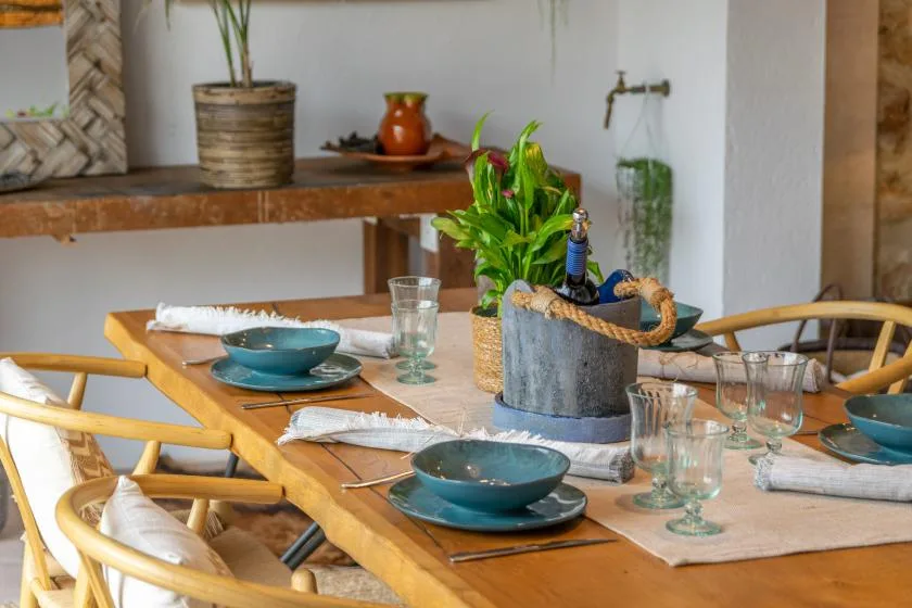 A dining table is set with dishes and greenery in a bright dining area.