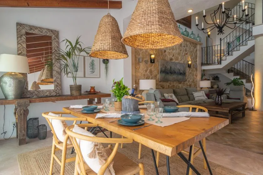 A dining area with a wooden table and woven pendant lights opens onto a living space.