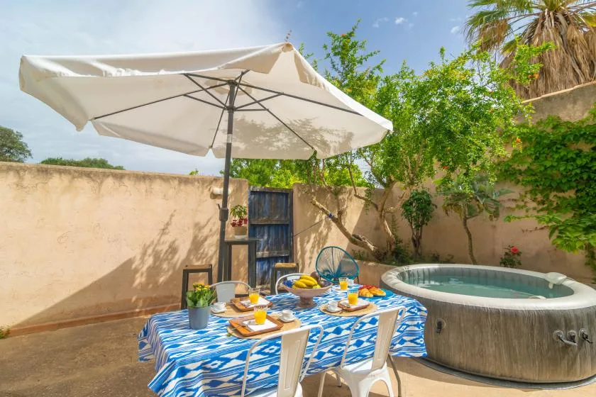 An outdoor dining table sits beneath an umbrella beside a round hot tub.