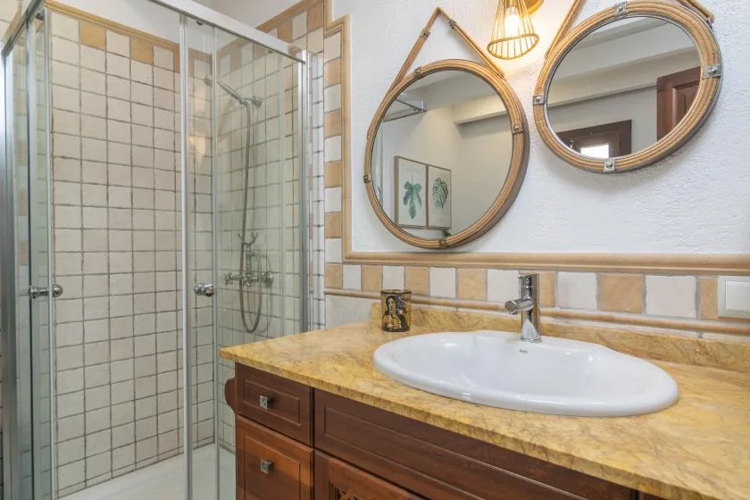 A bathroom with a glass shower, sink, and round mirrors above the vanity.