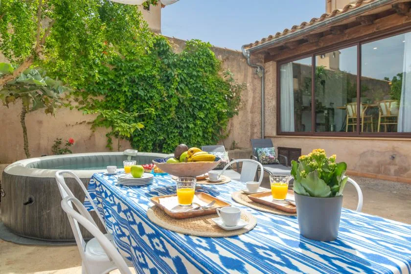 A patio dining area with a blue-patterned tablecloth, greenery, and a round tub.