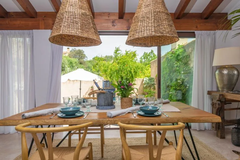 A dining area with a wooden table set beside large windows overlooking greenery.