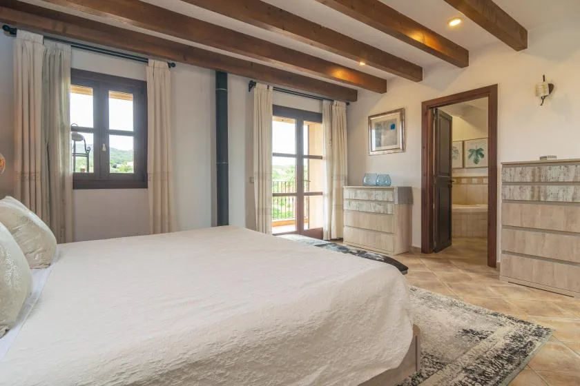 A bedroom with a large bed, exposed ceiling beams, and a doorway.
