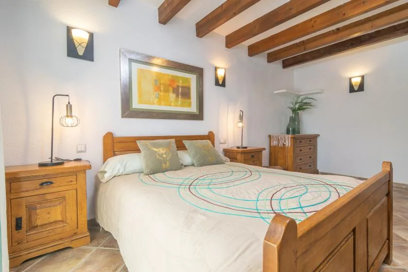 A bedroom with a wooden bed, bedside furniture, and exposed ceiling beams.