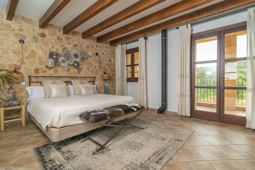 A bedroom with a large bed, stone walls, and wooden ceiling beams.