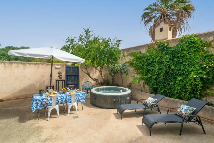An outdoor patio features a hot tub, dining table, and lounge seating beneath an umbrella.