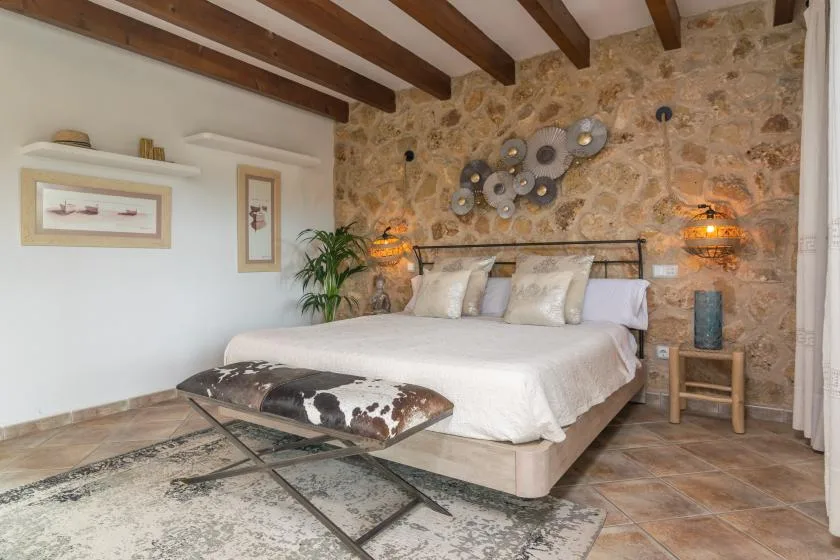 A bedroom with a large bed, stone wall, and exposed wooden ceiling beams.