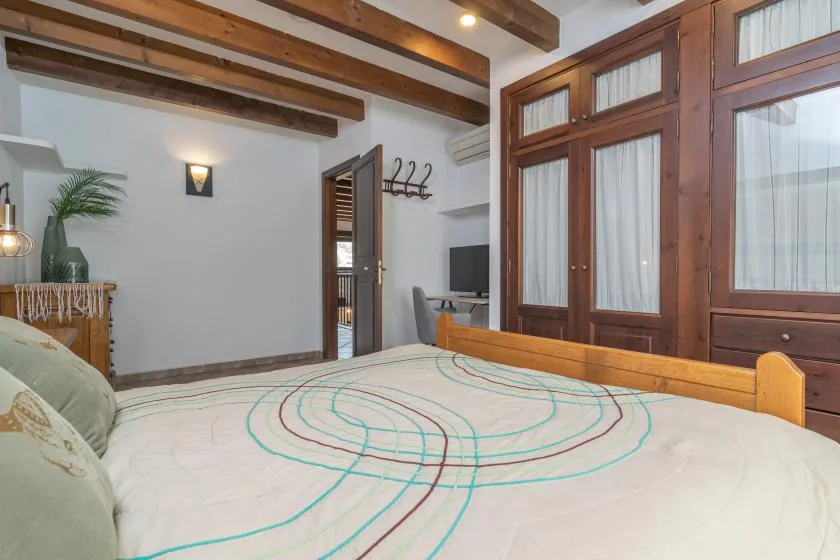 A bedroom with a large bed, exposed wooden ceiling beams, and tall wood-framed windows.