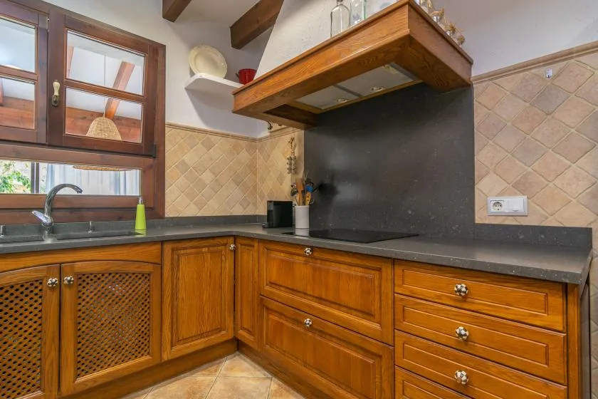 A kitchen with wooden cabinets, dark countertops, and a window above the sink.