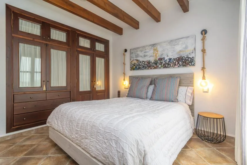 A bedroom with a large bed beneath exposed wooden ceiling beams.