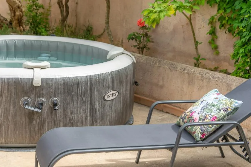 An outdoor patio with a round hot tub and a reclining lounge chair.
