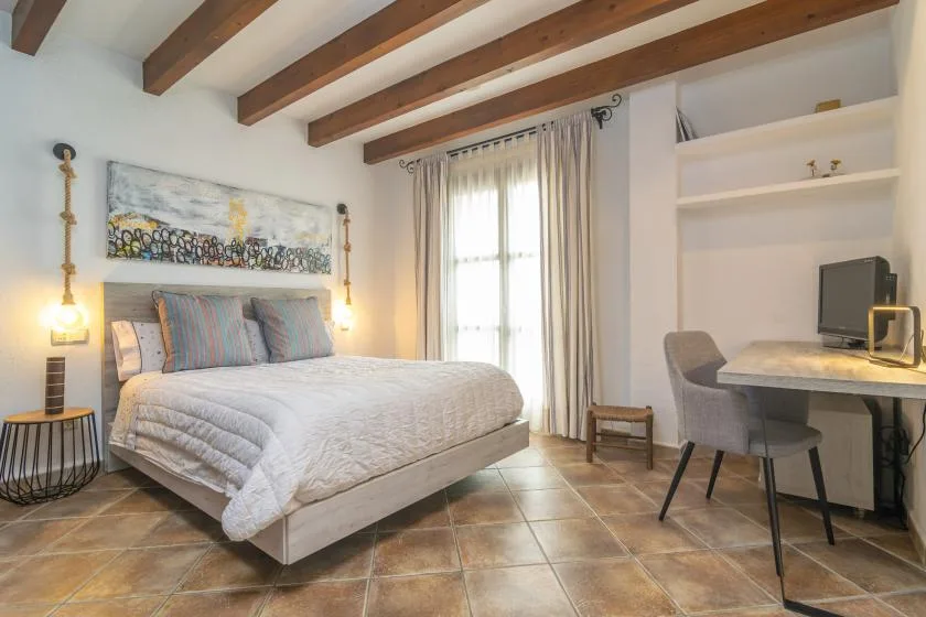 A bedroom with a bed, a desk, and a window with curtains.