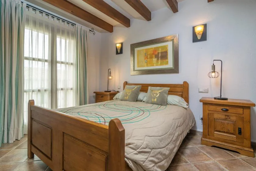 A bedroom with a wooden bed, bedside tables, and a large curtained window.