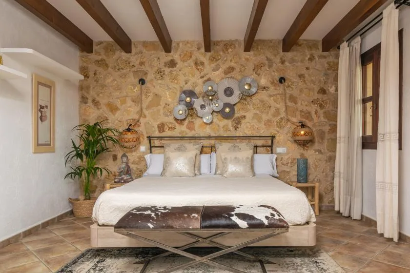 A bedroom with a bed against a stone wall and exposed ceiling beams.